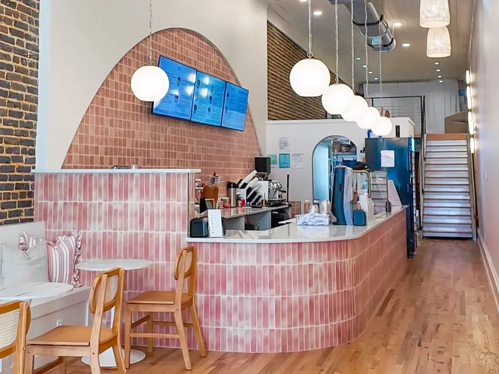 The counter inside a City Bowls shop, with pink tiled walls, globe pendant lights and digital menu boards